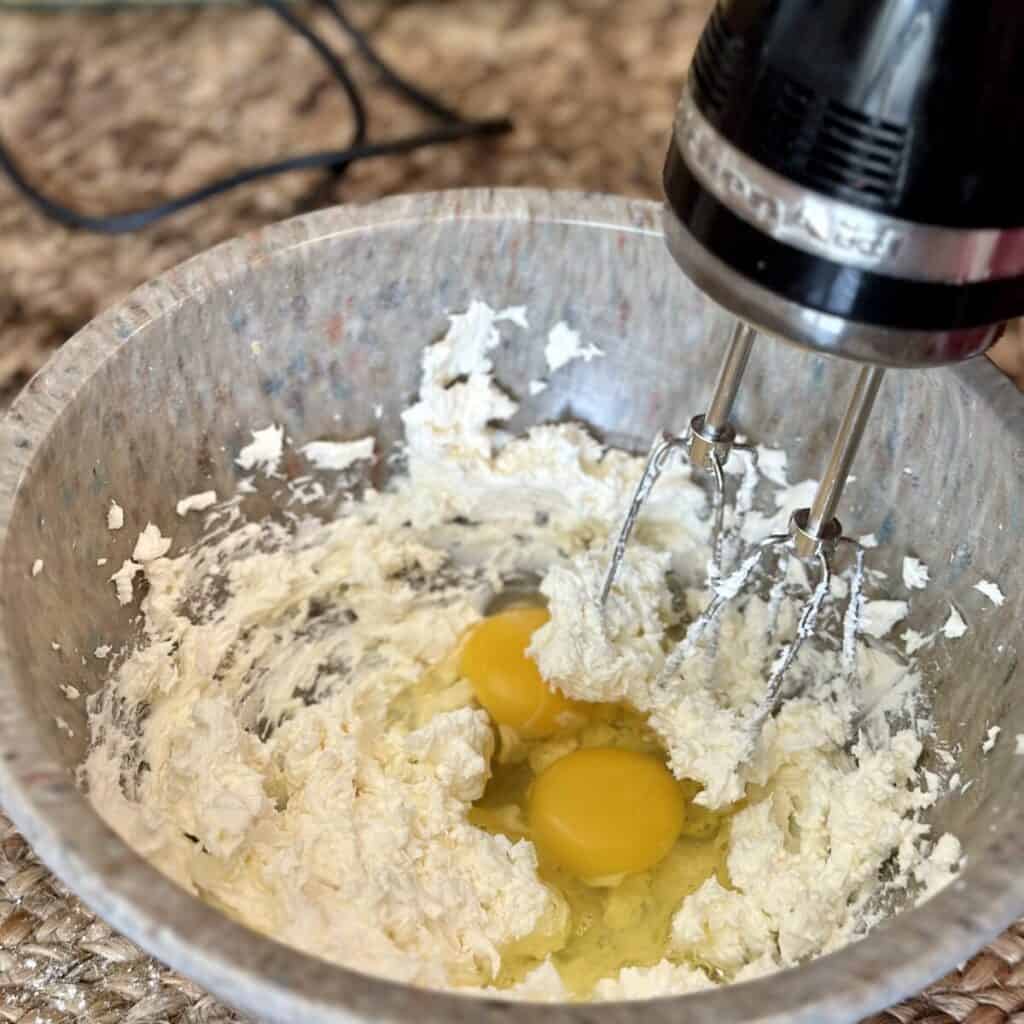 Whipping eggs in cream cheese in a bowl.