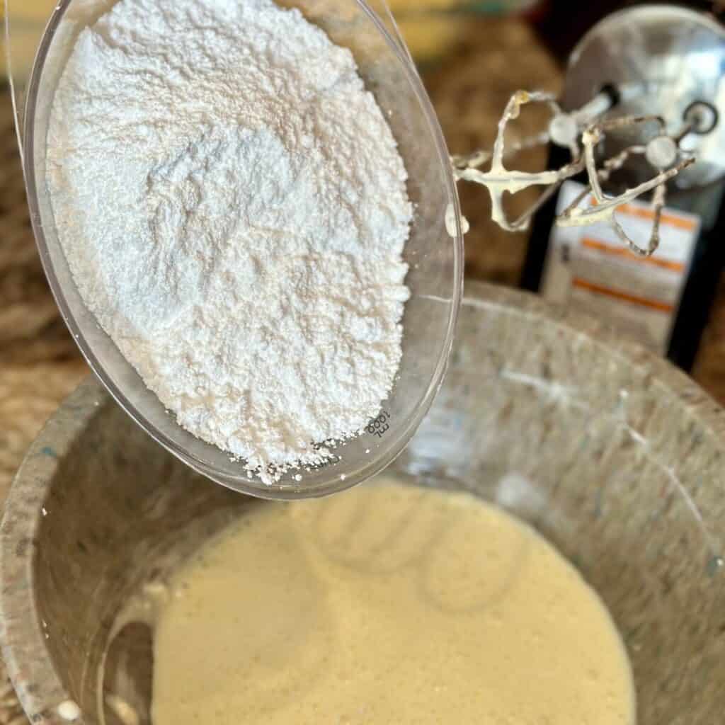 Adding powdered sugar to a bowl of dessert ingredients.