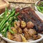 A plate topped with ribs, potatoes and green beans.