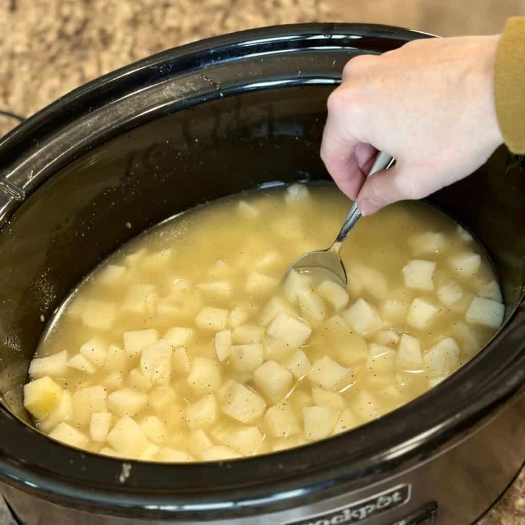 Mixing together ingredients for potato soup in a crockpot.