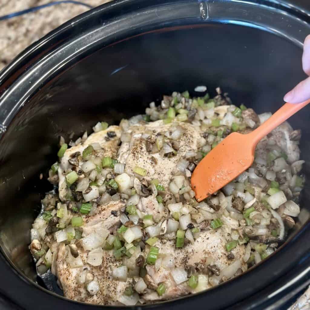 Adding vegetables to chicken in a crockpot.