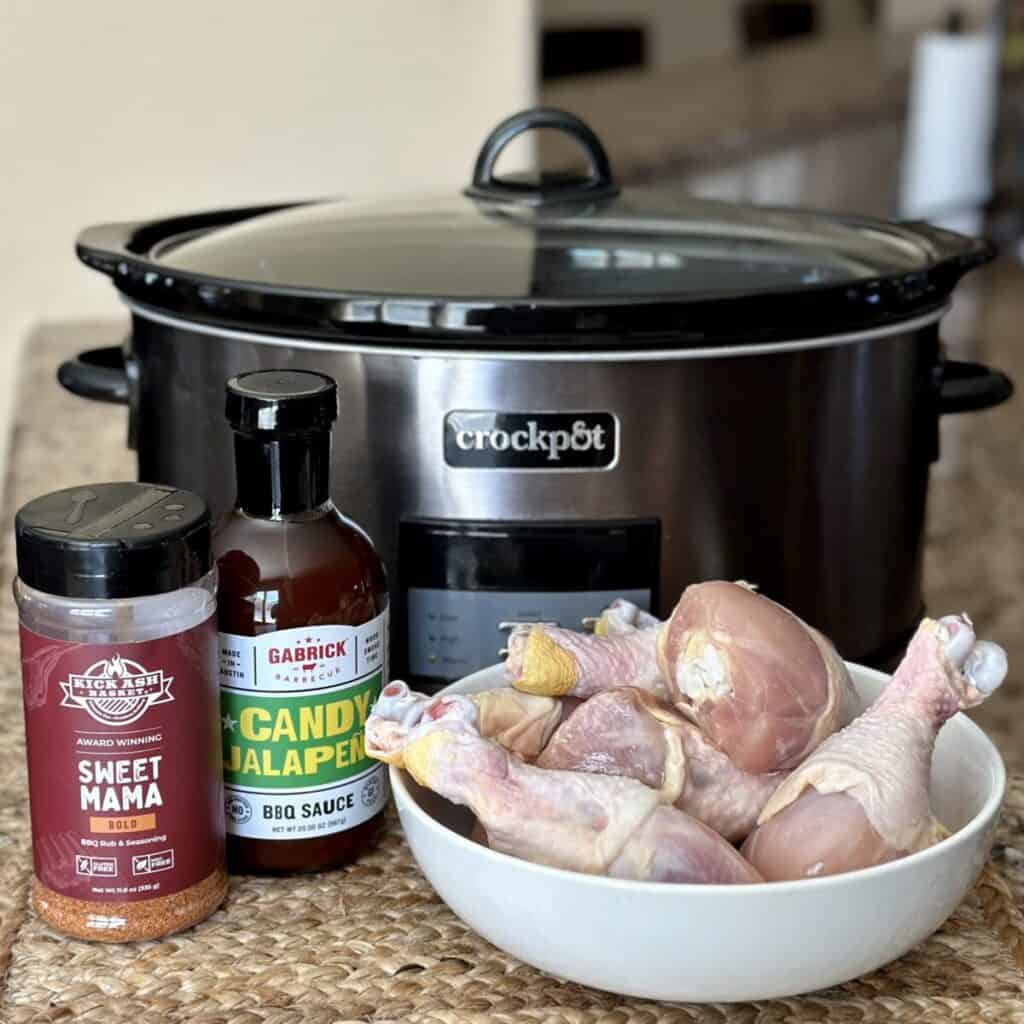 A crockpot with the ingredients to make bbq chicken legs.