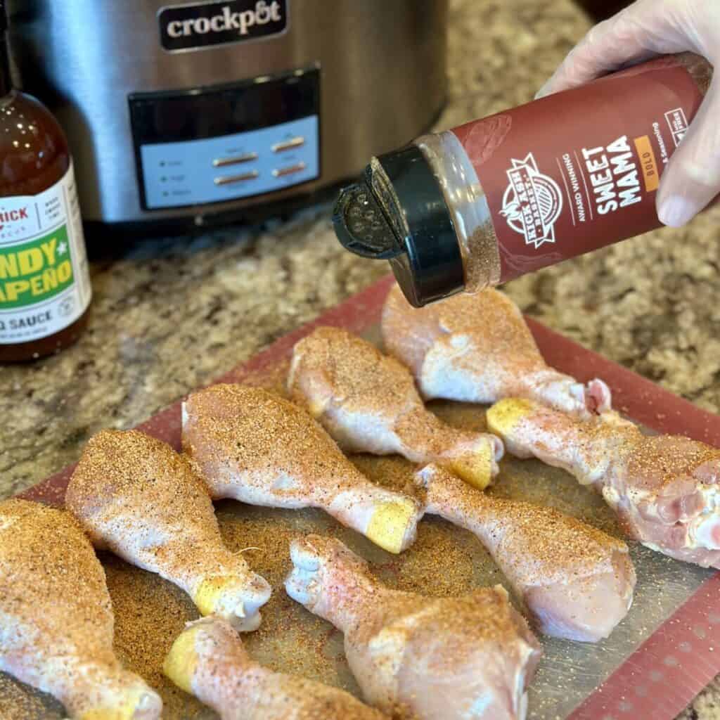 Adding bbq seasoning to chicken legs.