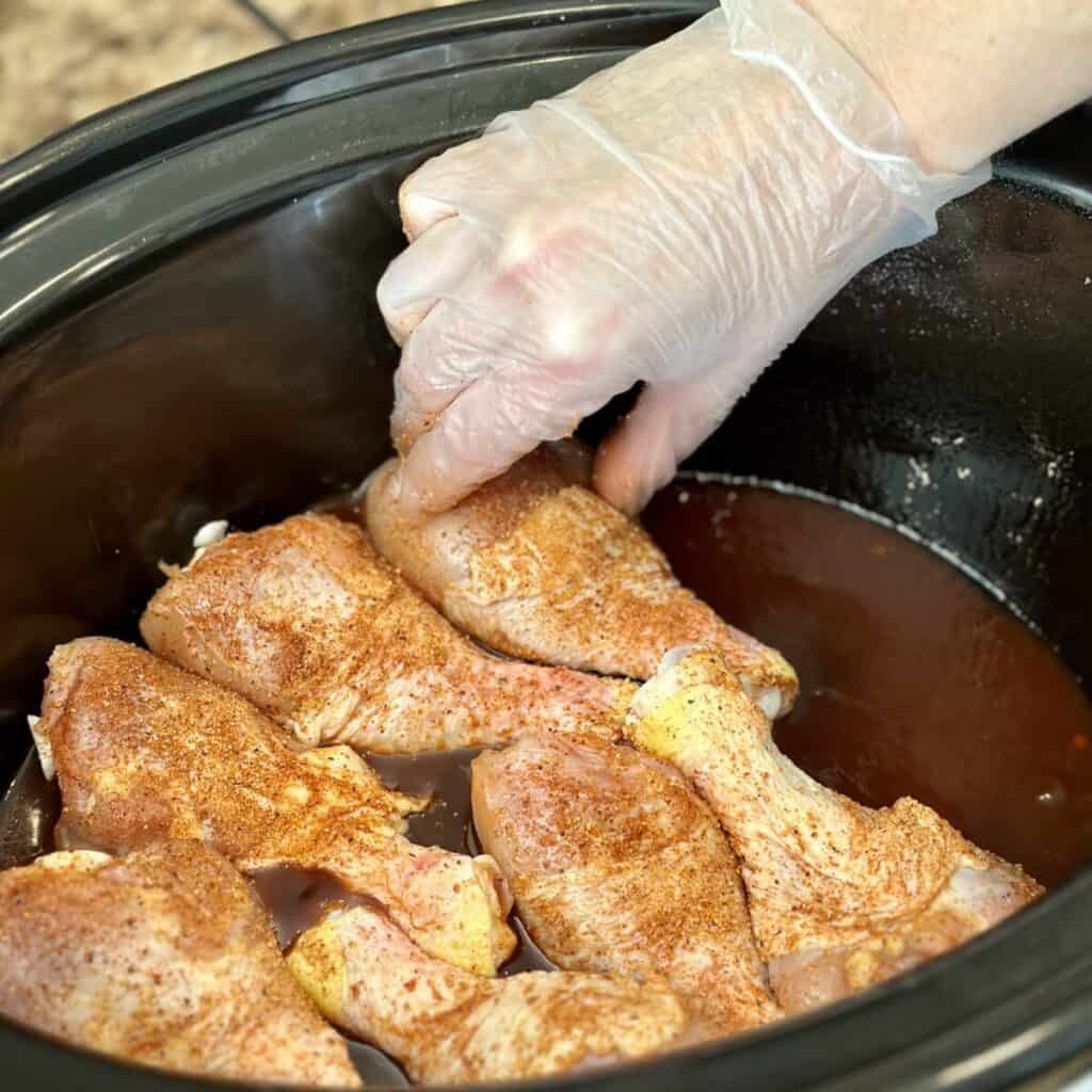 Adding seasoned chicken legs to a crockpot.