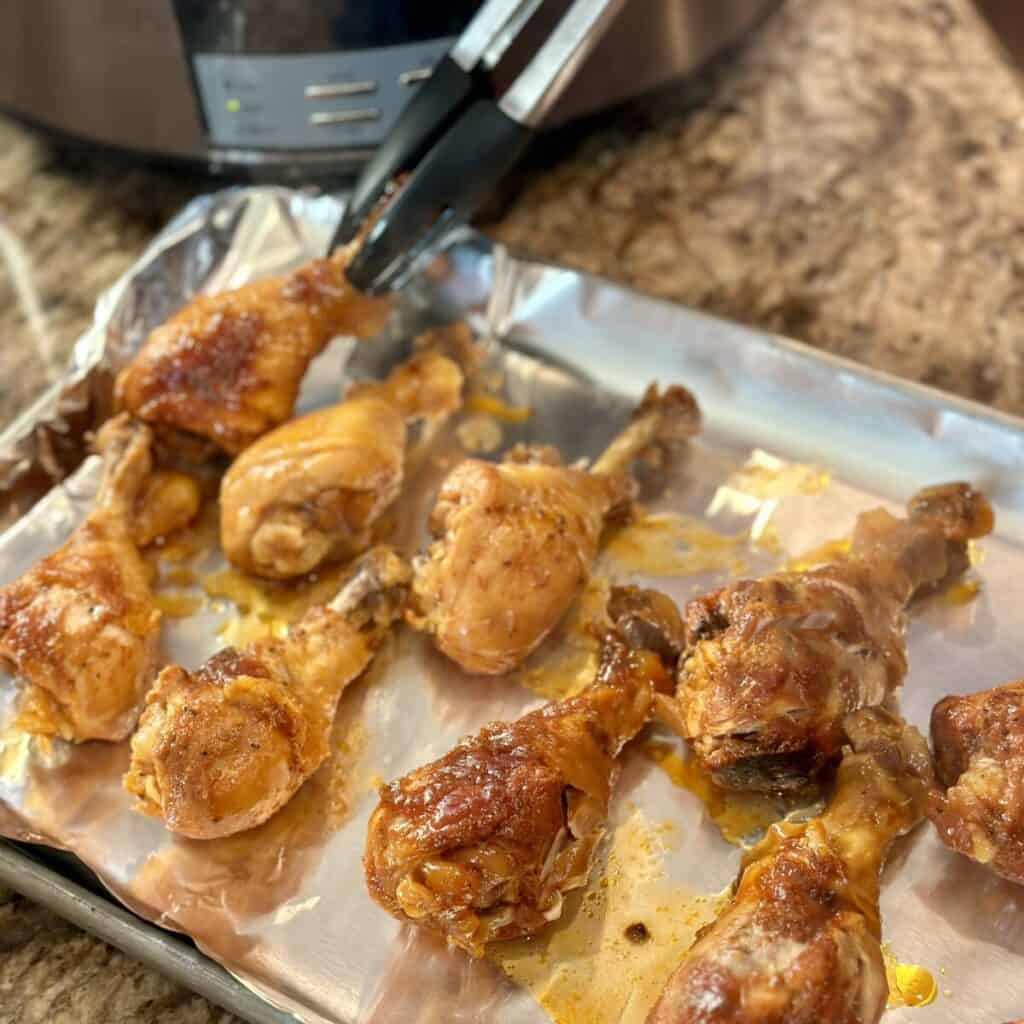 Putting cooking chicken legs on a sheet pan.