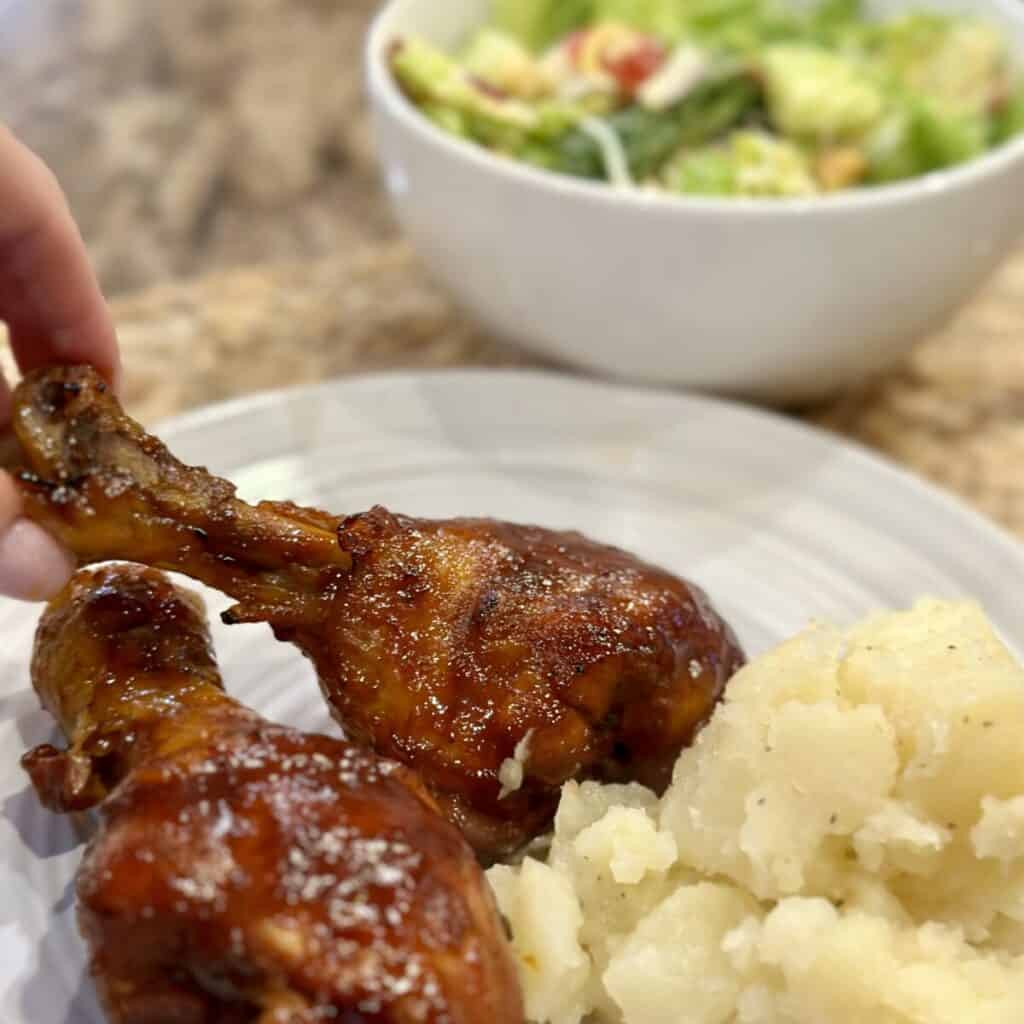 A plate with a barbecue chicken leg, potatoes and a salad.