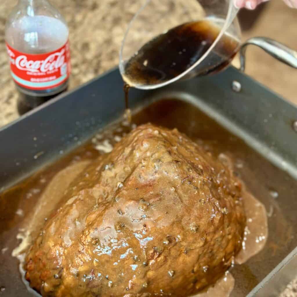 Pouring coke around a ham in a roasting pan.