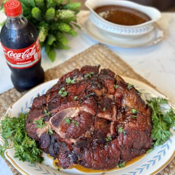 A ham on a serving tray garnished with parsley along side a coke that made the glaze.