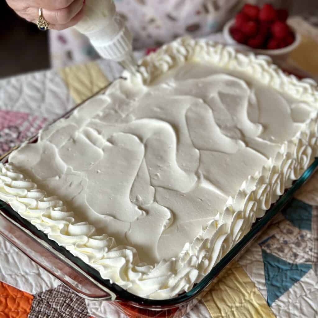 Adding whipped cream to the top of cake.