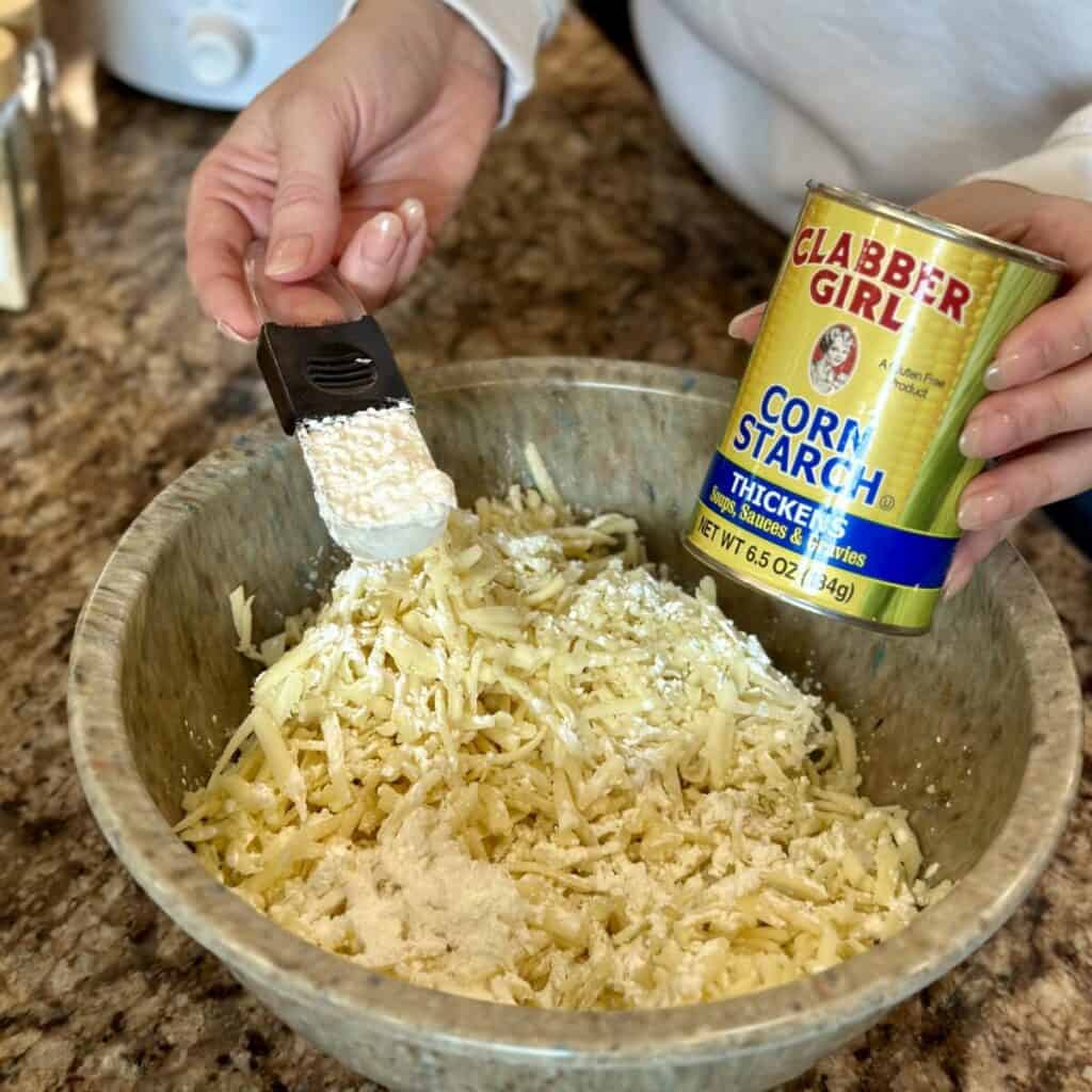 Adding cornstarch to shredded cheese in a bowl.