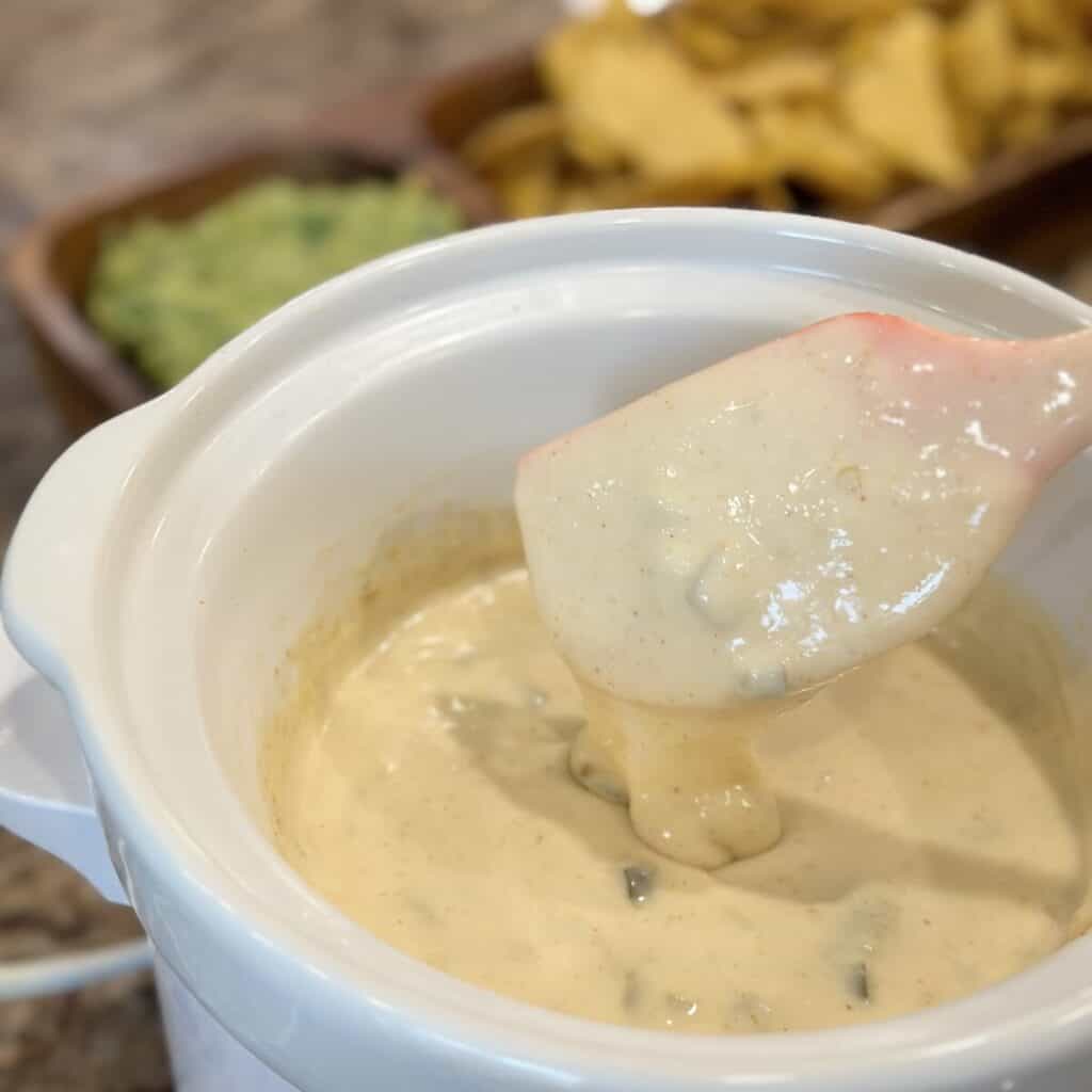 Stirring white queso dip in a crockpot.