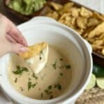 A chip dipping into a crockpot of white queso dip..