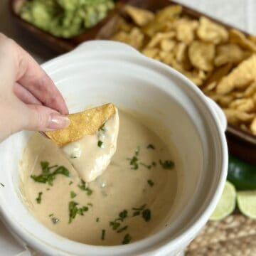 A chip dipping into a crockpot of white queso dip..