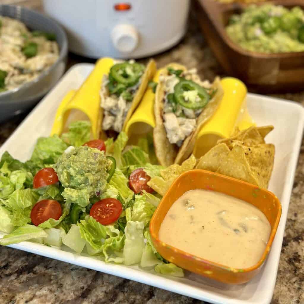 A plate of tacos, cheese dip, and salad with guacamole on top.