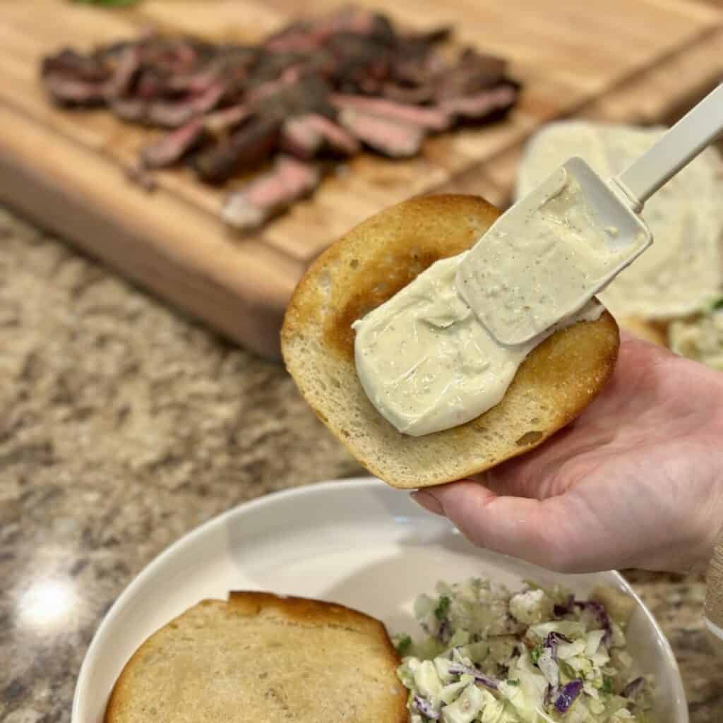 Spreading garlic aioli on a toasted roll.