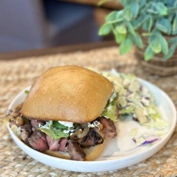 A ribeye steak sandwich and salad on a plate.