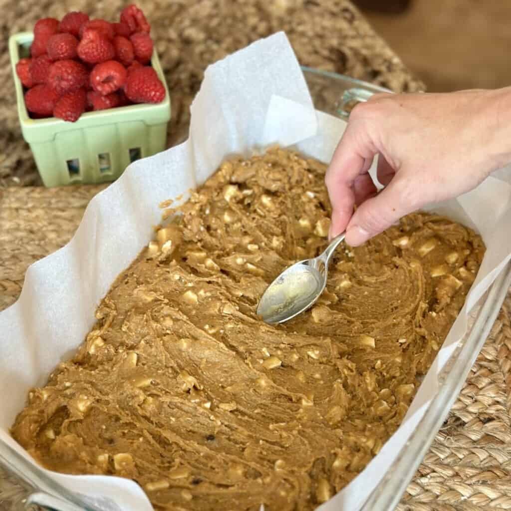 Spreading batter for white chocolate raspberry bars in a 13x9 dish.