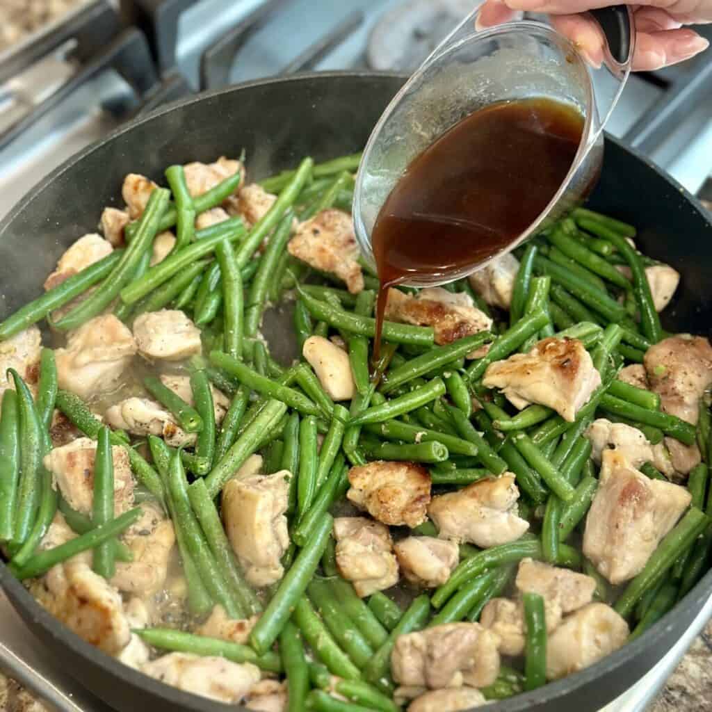 Adding sauce to a pan of chicken and green beans.