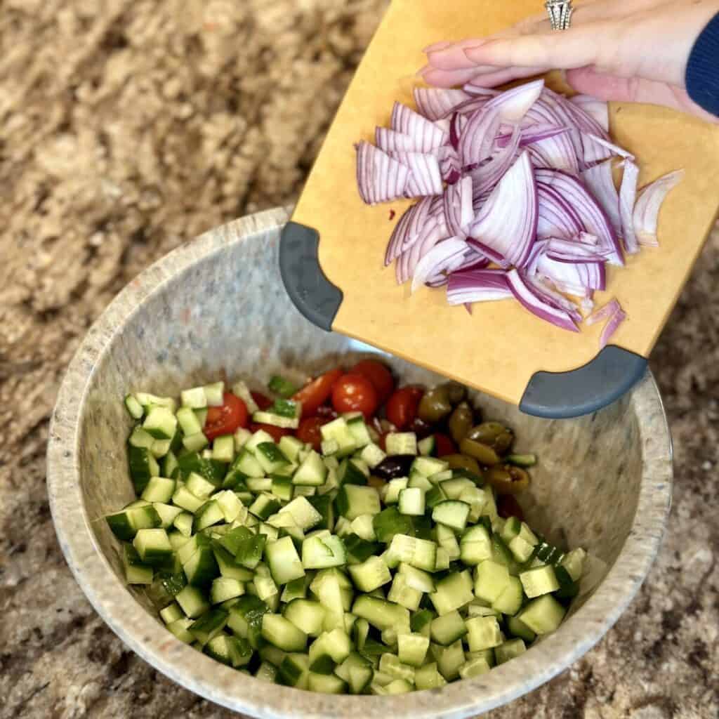 Adding red onion to a bowl of salad.