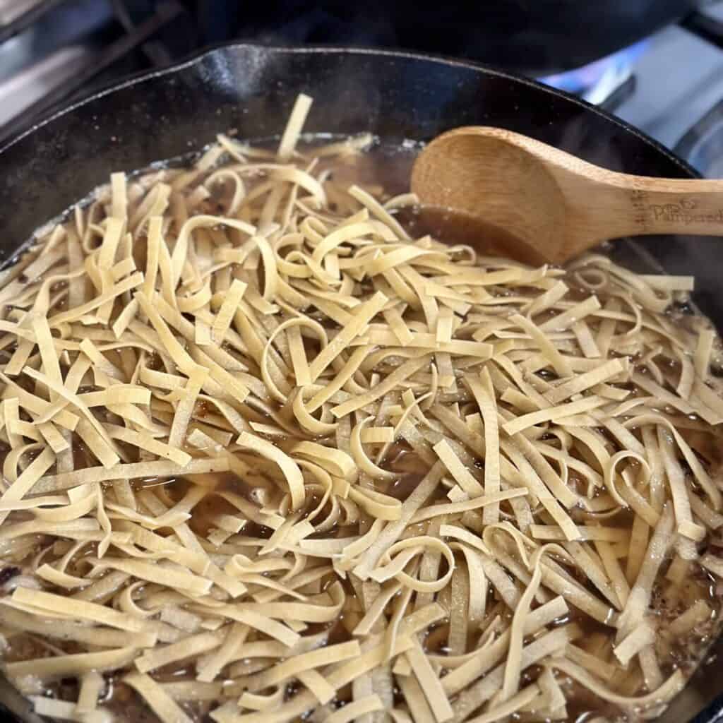 Cooking noodles in broth in a skillet.