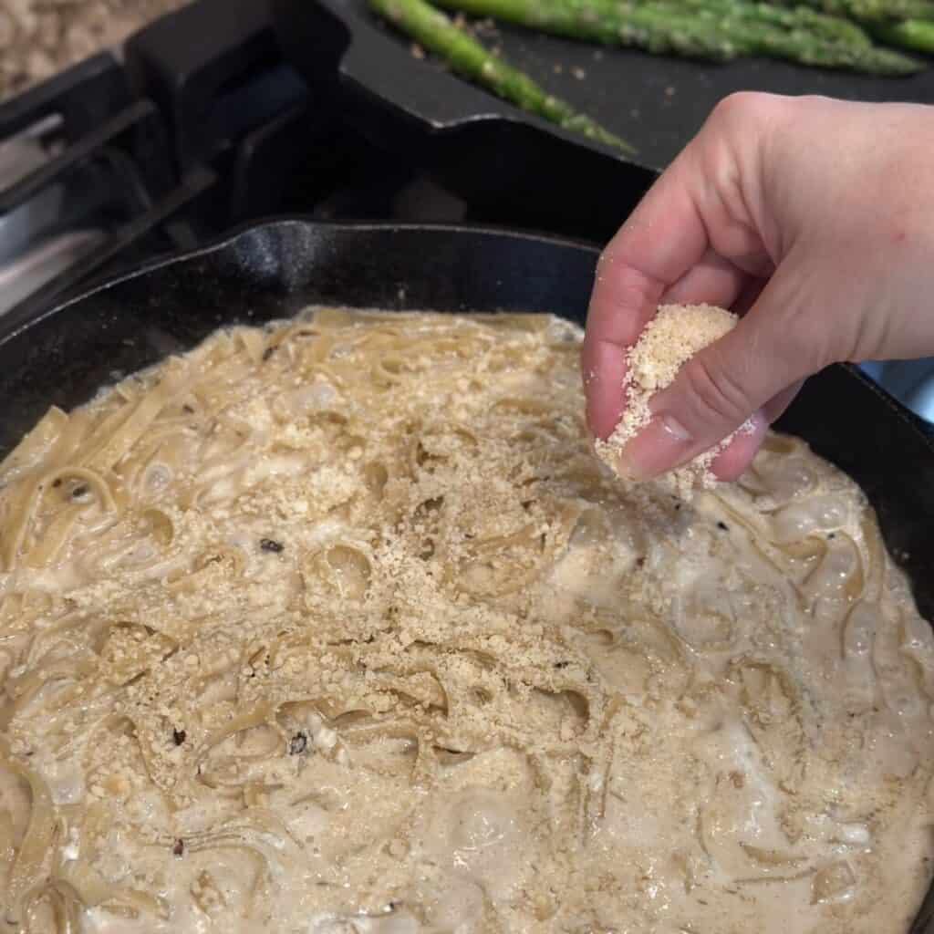 Adding parmesan cheese in a pan of pasta.