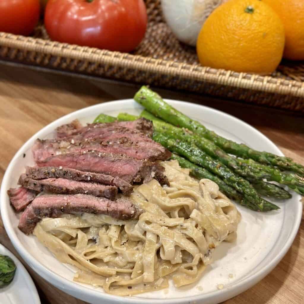 Pasta on a plate with steak and asparagus.