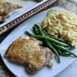 Skillet chicken thighs on a plate with green beans and noodles.