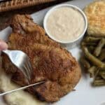 Cutting a fried pork chop on a plate of dinner.