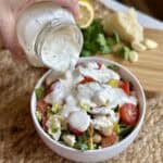 Pouring garlic salad dressing on a salad.