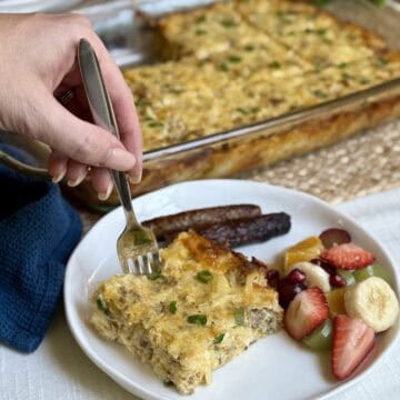 A slice of Amish breakfast casserole, fruit and sausage on a plate.