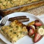 A slice of Amish breakfast casserole, fruit and sausage on a plate.