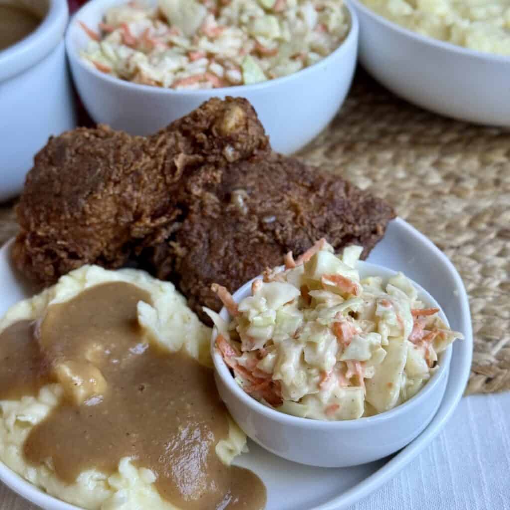 A plate of copycat KFC coleslaw, mashed potatoes and gravy and fried chicken.