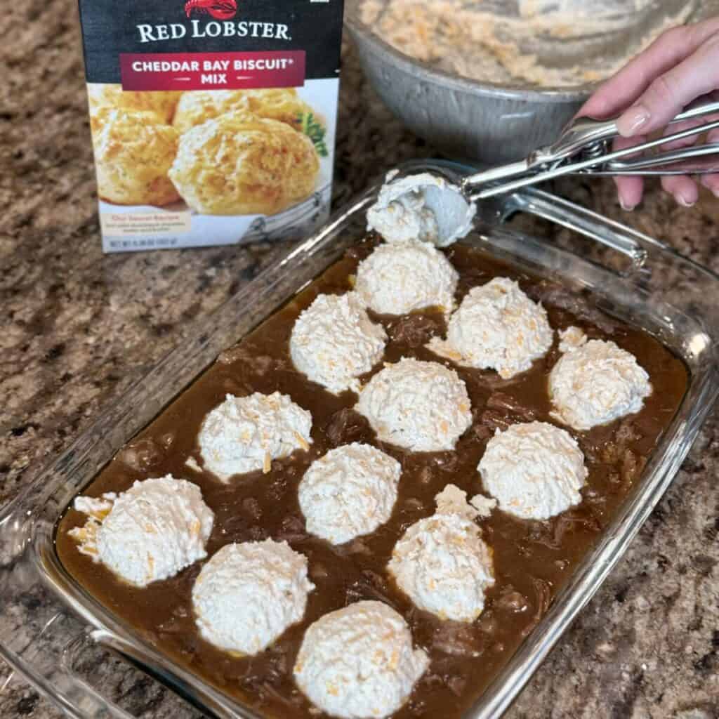 Scooping biscuit dough on a beef and gravy.