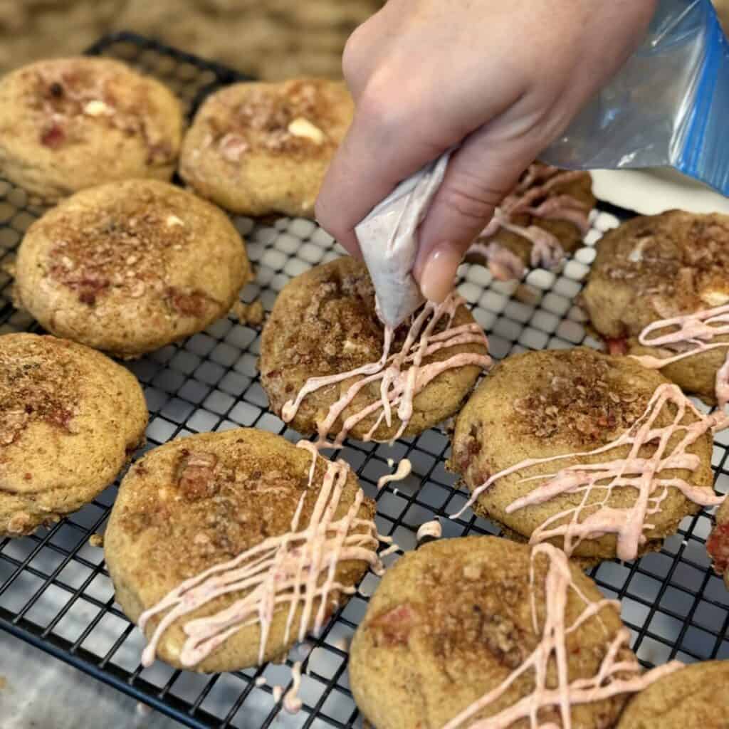 Adding white chocolate drizzle to the top of strawberry shortcake cookies.