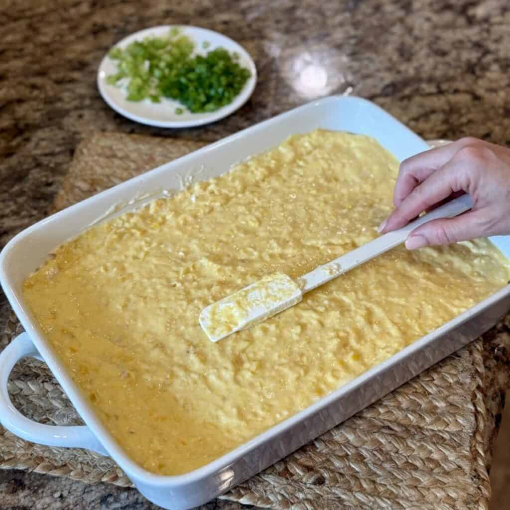 Spreading the cornbread layer of chicken cornbread casserole in a dish.
