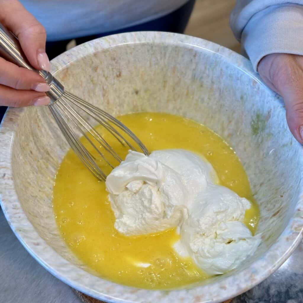 Whisking together the ingredients in a bowl for cheesy corn casserole.