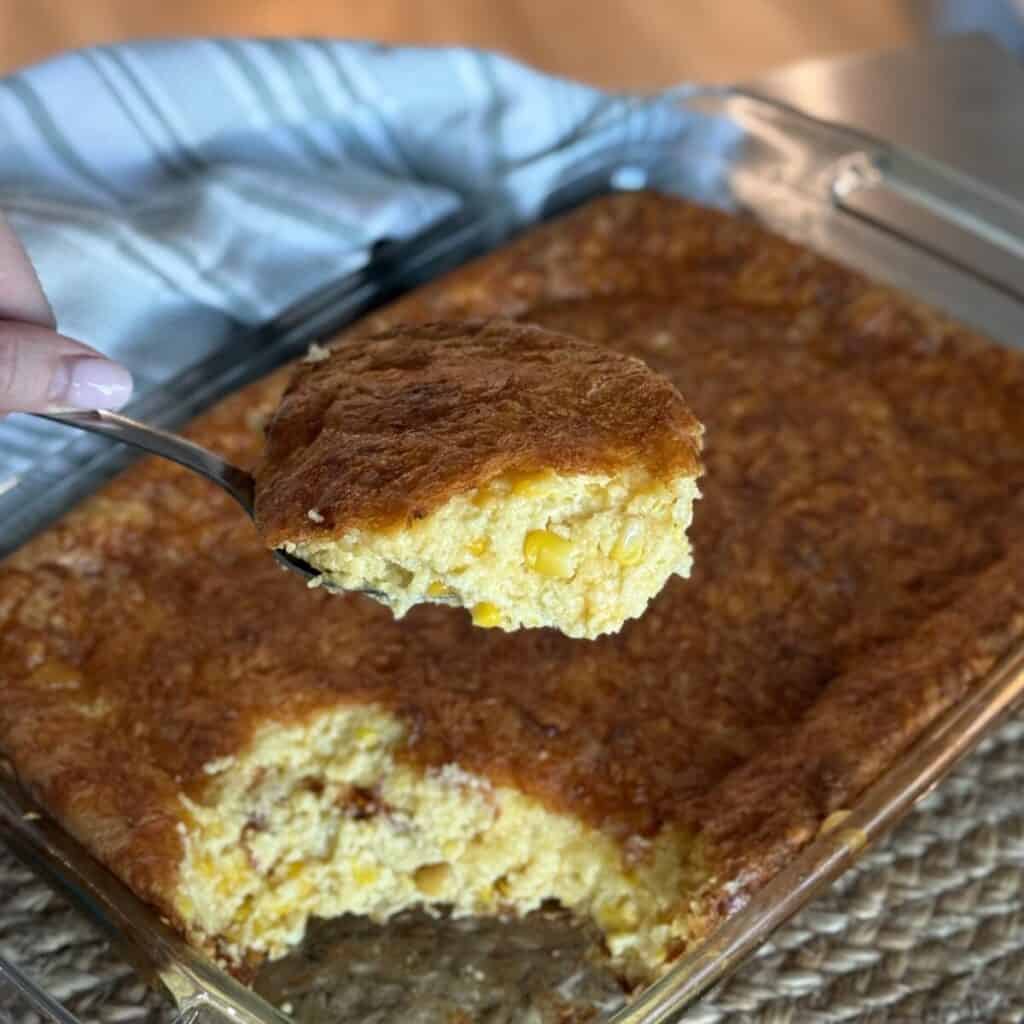 A spoonful from a pan of cheesy corn casserole.