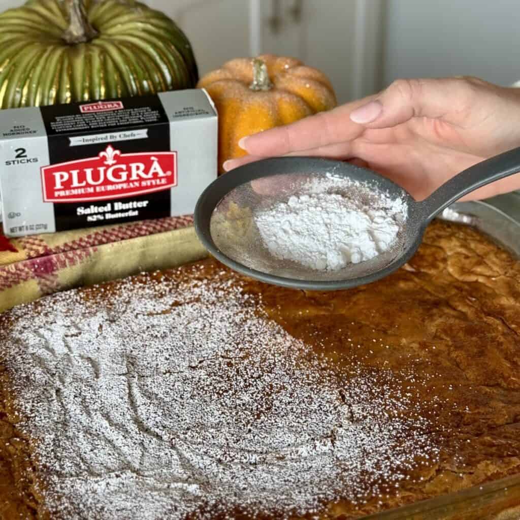Sprinking powdered sugar on pumpkin gooey butter cake.