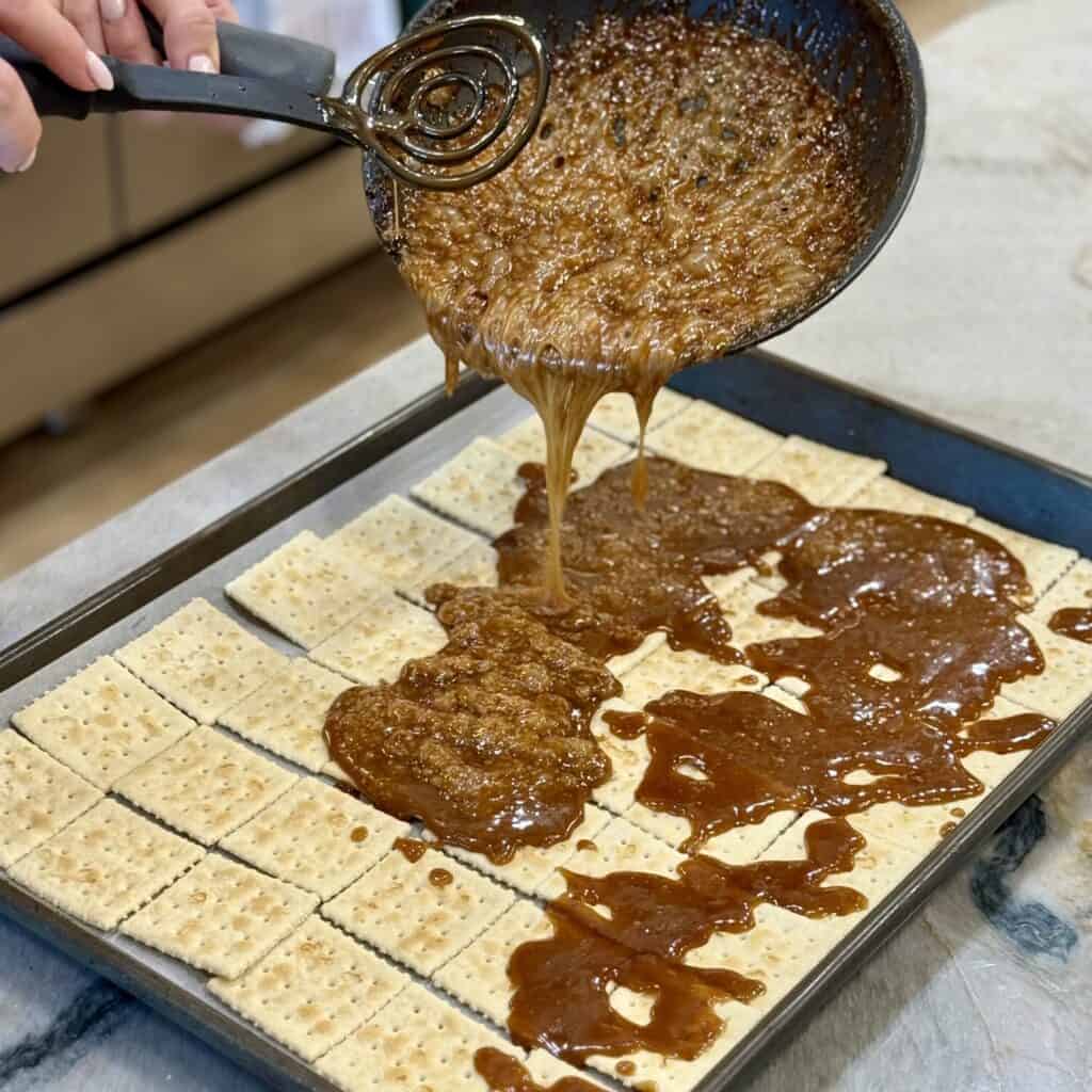 Pouring praline on crackers on a sheet pan.