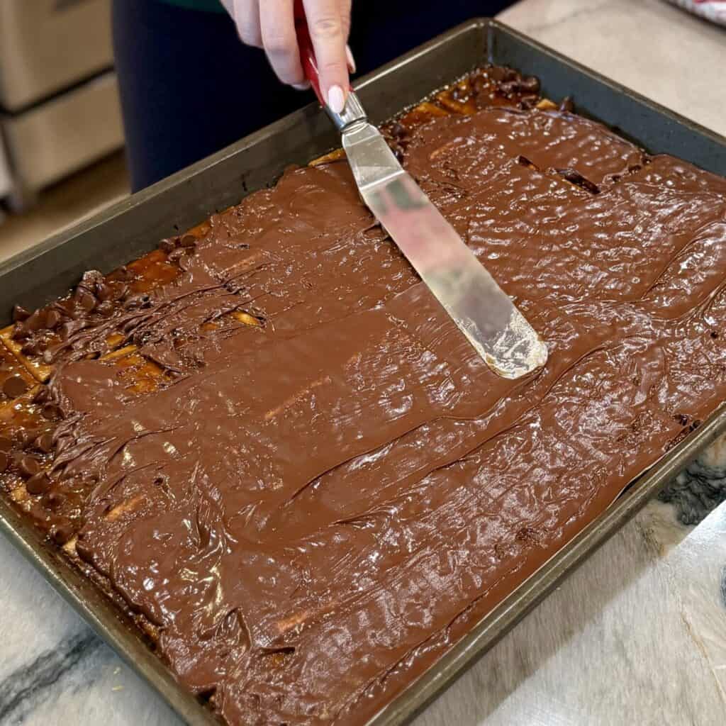 Spreading chocolate on toffee on a sheet pan.