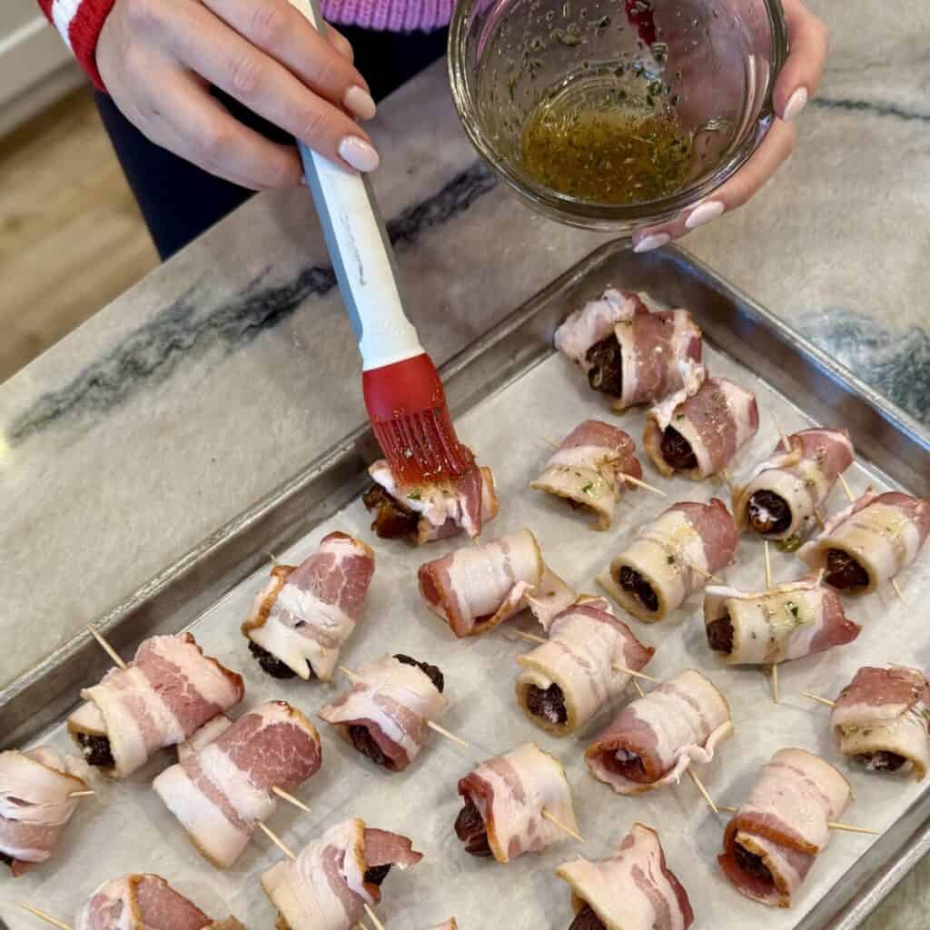 Brushing bacon wrapped dates with honey.