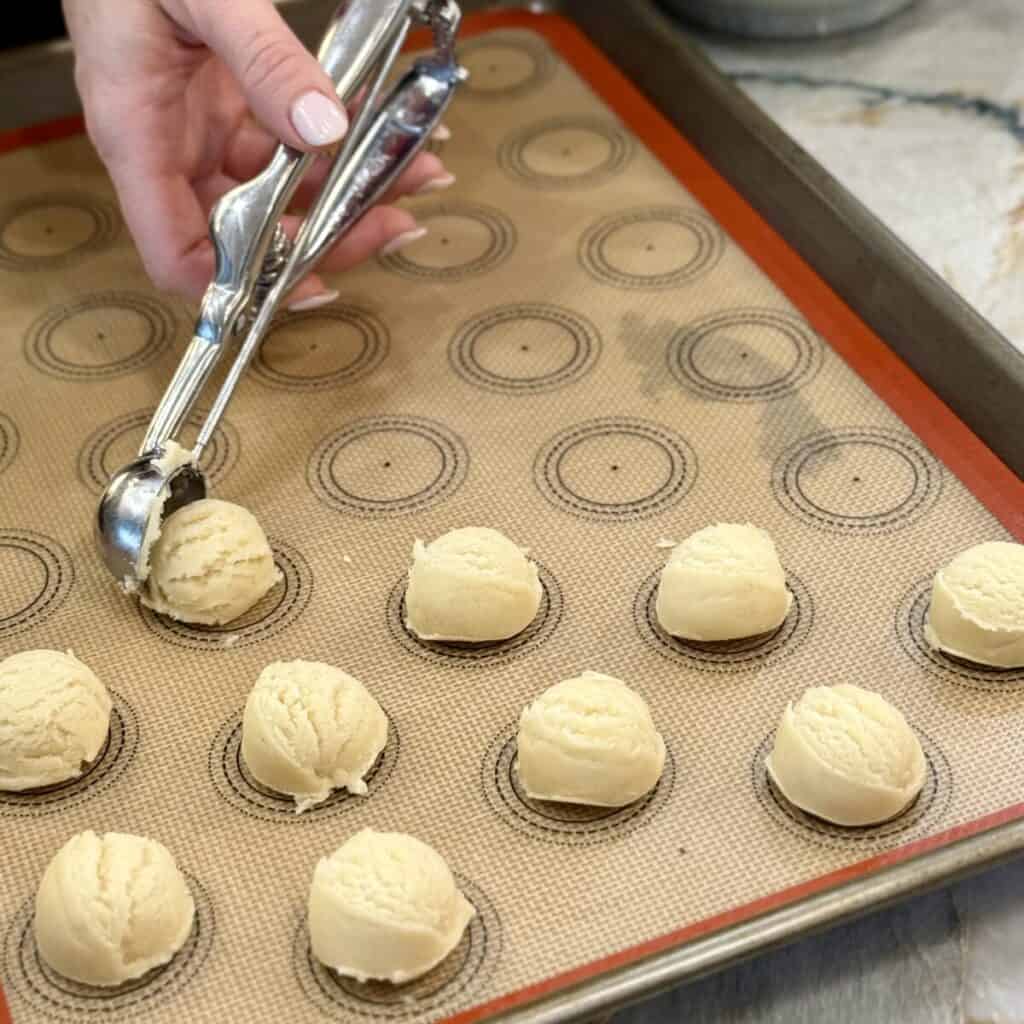 Scooping out raspberry thumbprint cookie dough on a sheet pan.