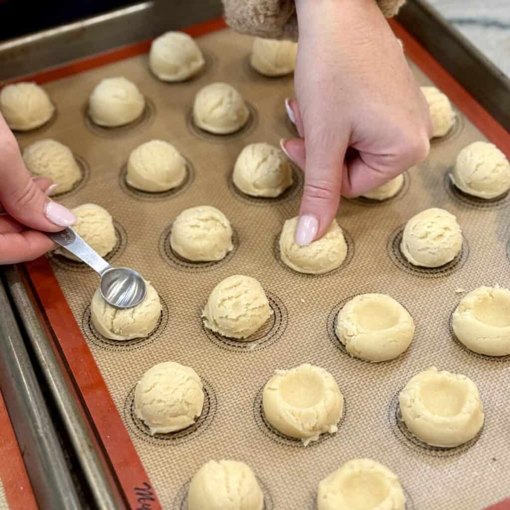 Making indentions in raspberry thumbprint cookie dough on a sheet pan.