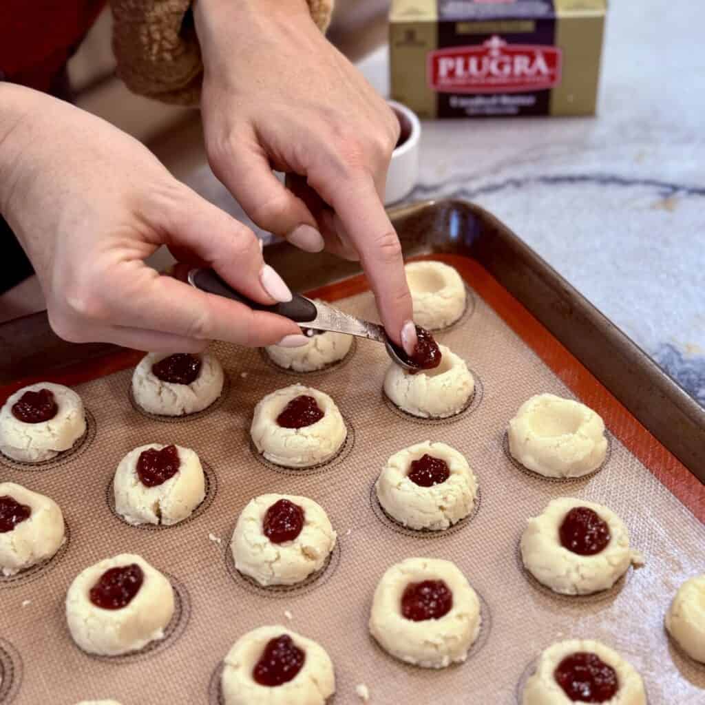 Adding jam to the center of raspberry thumbprint cookies. 