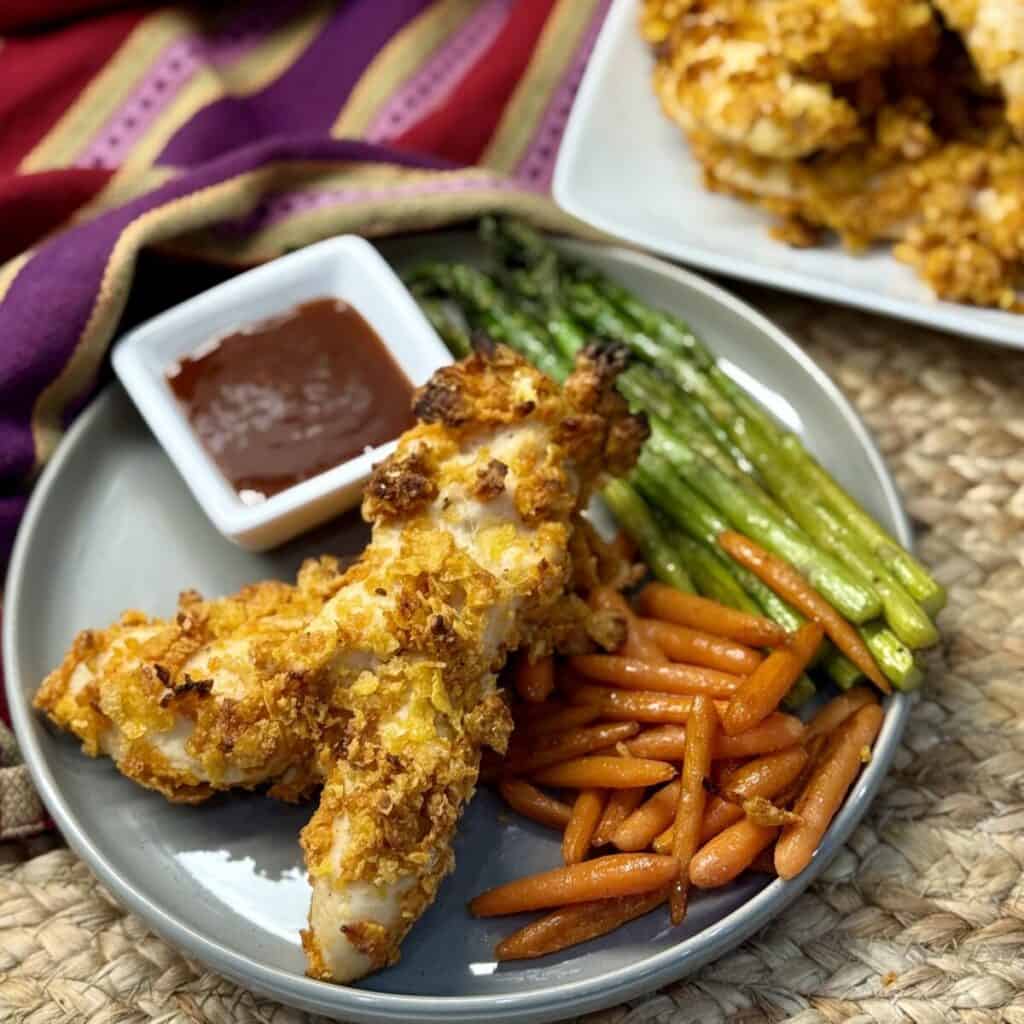 A plate of cornflake chicken tenders, carrots and asparagus. 