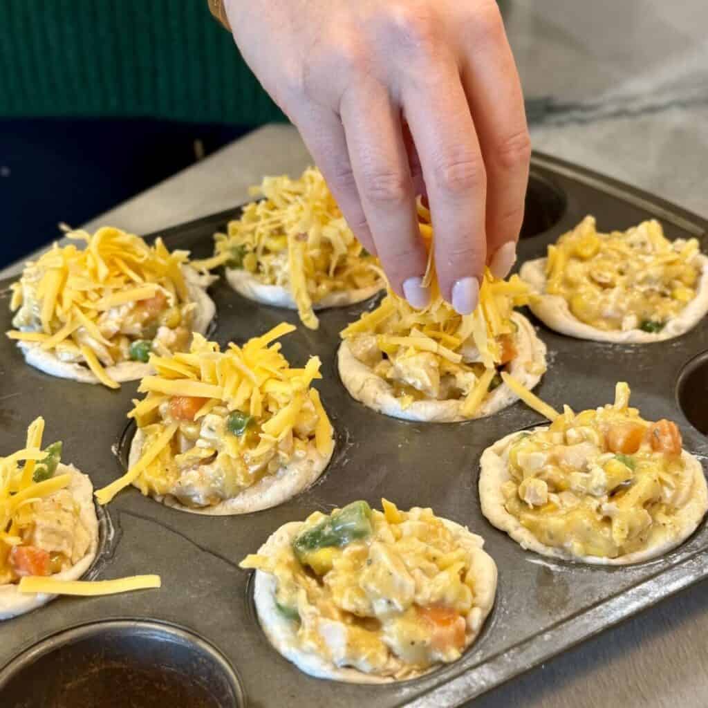 Adding cheese to the top of mini chicken pot pie.