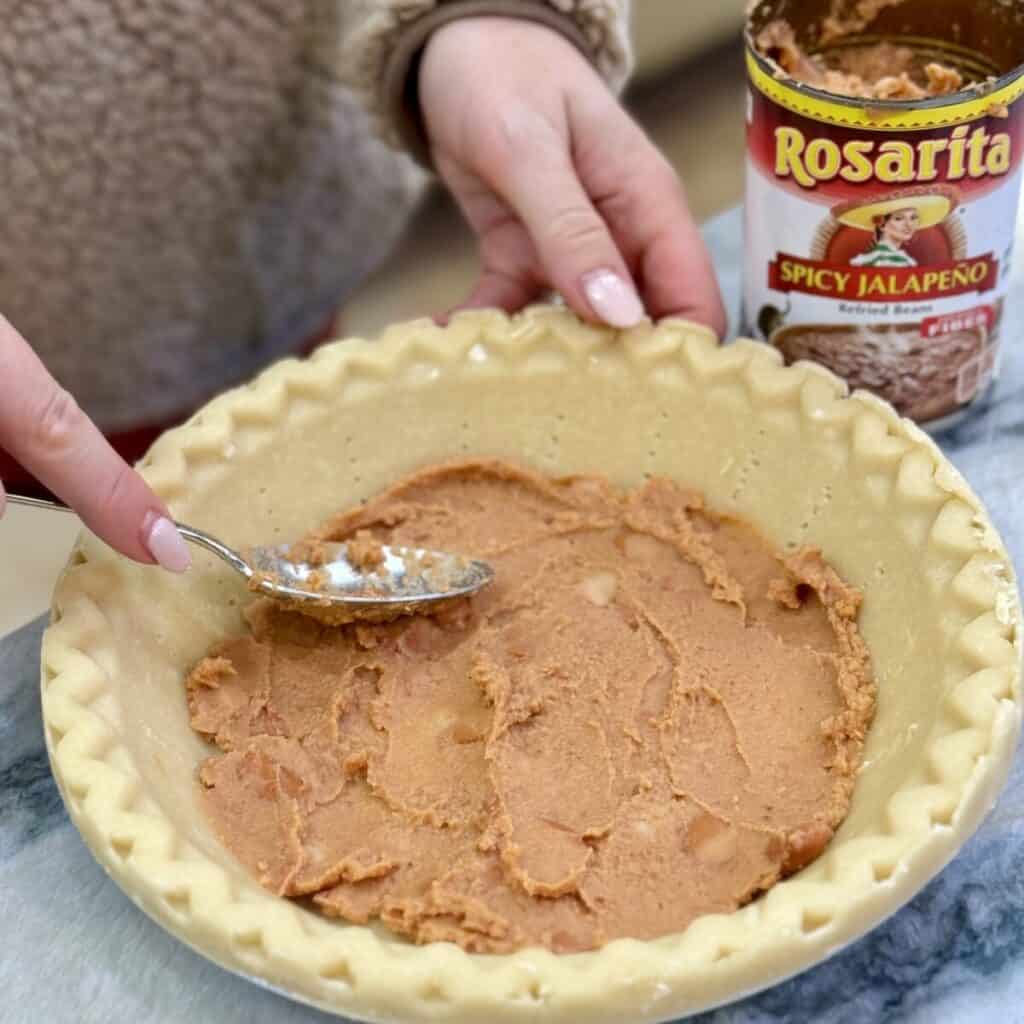 Spreading refried beans in a pie crust.