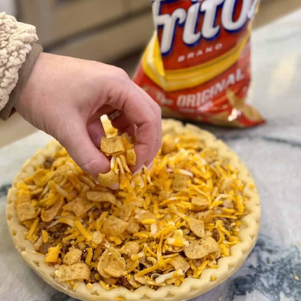 Adding cheese and chips on top of a beef filling to a pie crust.