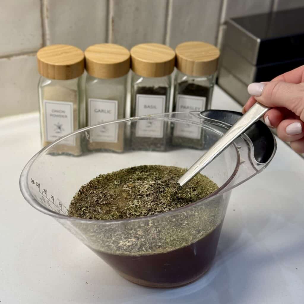 Mixing together beef broth and dried herbs in a measuring cup.