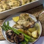 A plate of roasted chicken thighs and potatoes with asparagus.